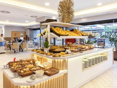 Area colazione luminosa con buffet di pasticceria e cibi freschi in hotel moderno.