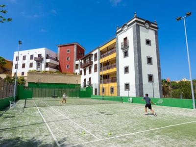 Tenisový kurt před barevnými obytnými budovami pod jasnou oblohou