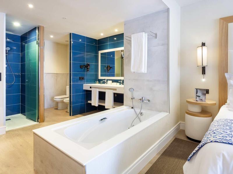 Camera d'hotel moderna con vasca da bagno, doccia, doppi lavandini e camera adiacente.