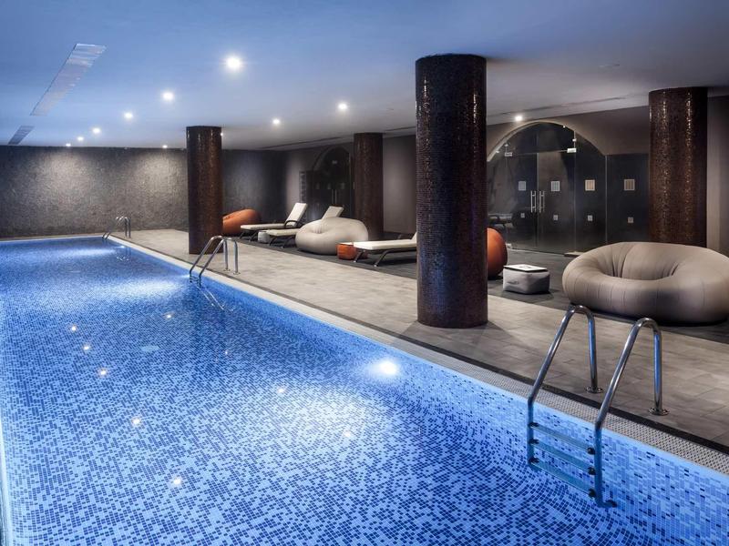 Piscina interna moderna con piastrelle a mosaico, comodi posti a sedere e illuminazione d'ambiente.