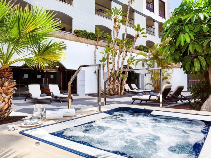 Vasca idromassaggio su una terrazza d'hotel con lettini e palme.