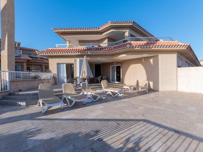 Terraza con tumbonas y sombrillas frente a una casa clara bajo un cielo azul.