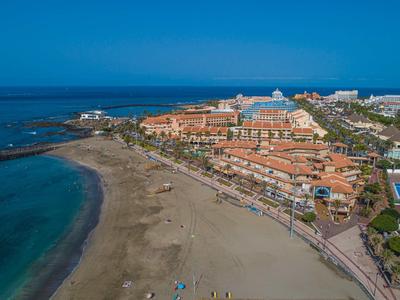 View of a large sandy beach with hotels and promenade along the coast under clear skies.