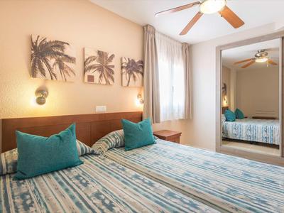 Bright hotel room with two beds, turquoise pillows, and palm wall art.