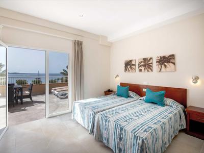 Bright hotel room with two single beds, balcony access, and sea view.