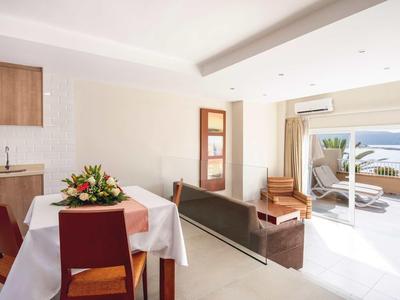 Bright hotel room with dining area, sofa, and access to a terrace with sea view.
