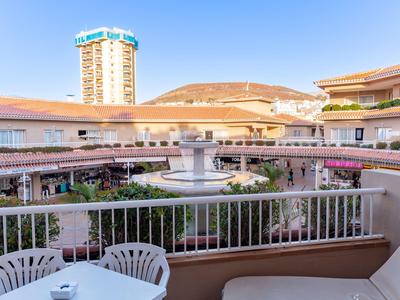 Vista desde un balcón con mesa y sillas hacia un patio con fuente y edificios alrededor.