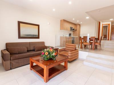 Sala luminosa con sofá marrón, mesa de centro de madera y escalones hacia el comedor con mesa y sillas de madera.