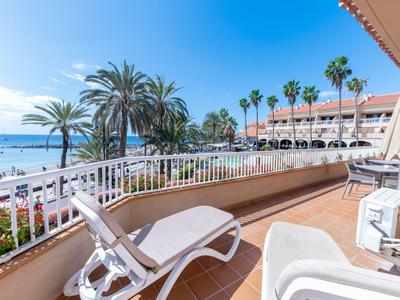 Balcón con tumbona con vista a la playa, el mar y palmeras en un día soleado.