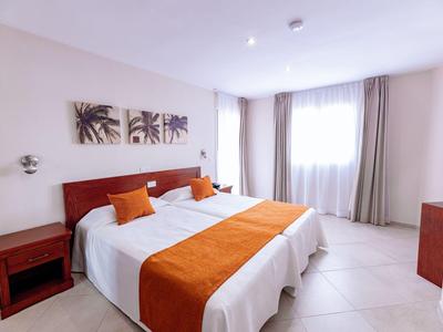 Habitation de hotel iluminada con dos camas individuales y acentos naranjas