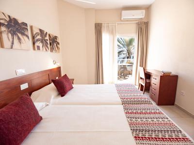 Habitación de hotel luminosa con dos camas individuales y vista al balcón.