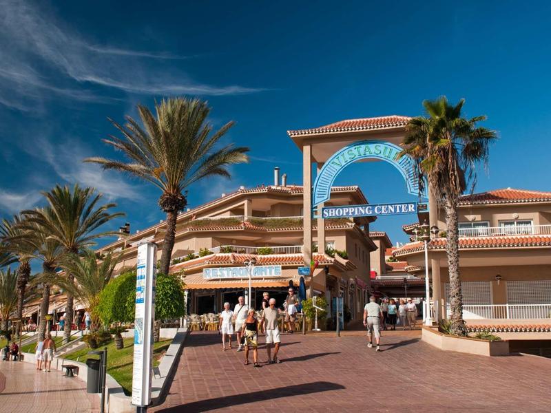 Hotel with outdoor terrace and palm trees under clear blue sky.