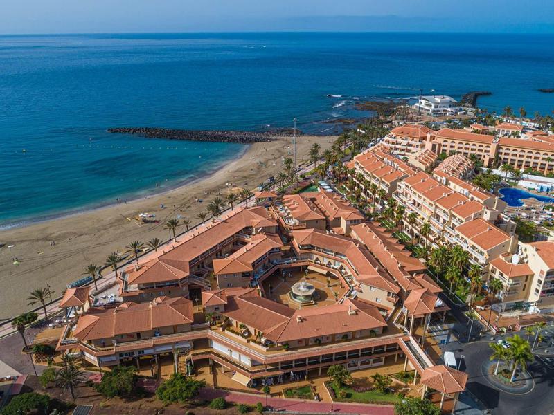Aerial view of a resort with terracotta roofs by the beach and blue lagoon.