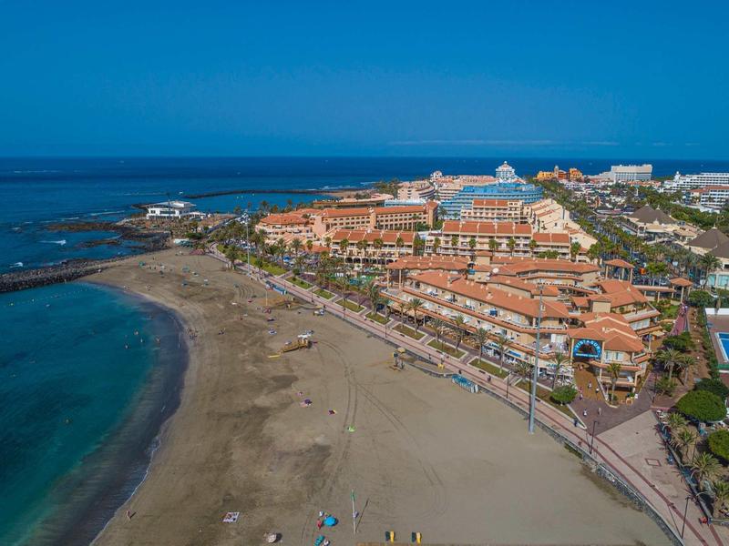 View of a large sandy beach with hotels and promenade along the coast under clear skies.