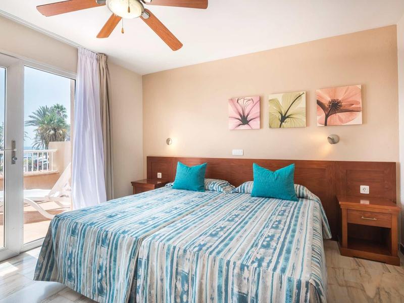 Bright hotel room with two single beds, turquoise pillows, and access to the terrace.