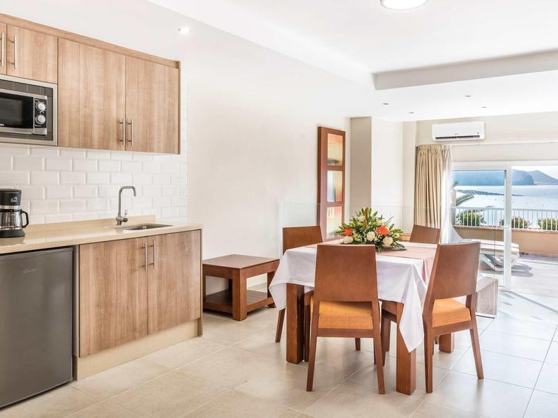 Bright dining area and kitchenette with view of terrace and sea in a hotel room.