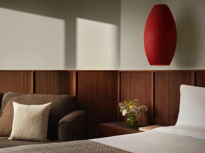 Modernes Schlafzimmer mit braunem Sofa, weißem Kissen, Holzwand, Nachttisch und roter Lampe.