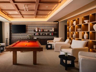 Una sala de juegos acogedora con mesa de billar, sillones cómodos y estantes decorativos en la pared.