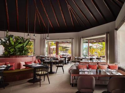 Modernes Restaurant mit runder Decke, Pflanzenwand, runden und rechteckigen Tischen, hellen Stühlen.