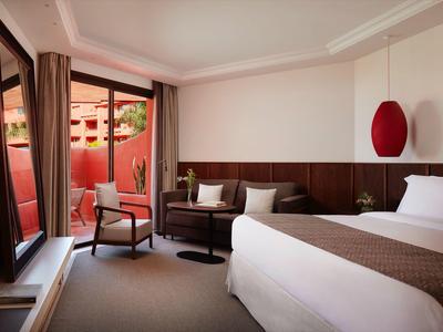 Helles, modernes Schlafzimmer mit großem Bett, Sofa, Stuhl und Zugang zu einer Terrasse mit Pflanzen.