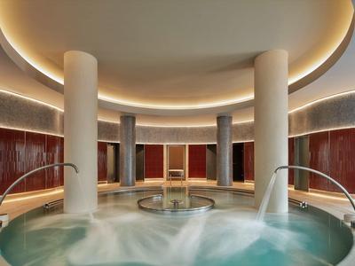 Runder Pool mit Wasserspielen, Säulen und warmem, indirektem Deckenlicht in modernem Spa.