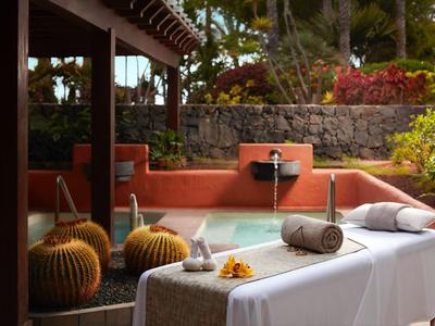 Entspannungsbereich mit Massagebank, Kopfstütze, Pflanzen, Steinen und Holzstruktur im Garten.