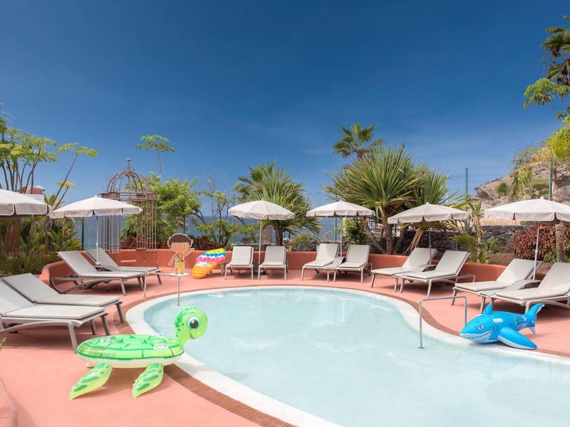 Kleiner Pool mit Liegestühlen, Sonnenschirmen, roten Terrakotta-Fliesen und aufblasbaren Spielzeugen.