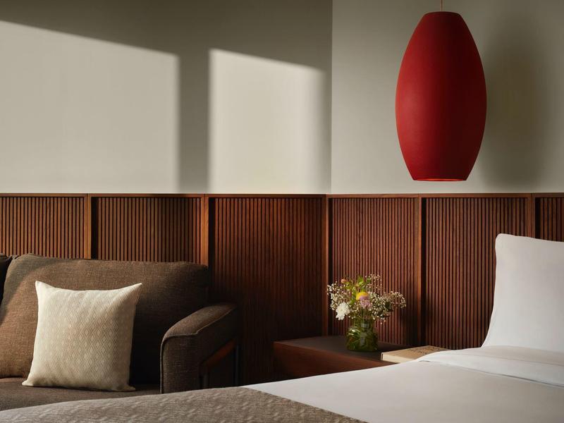 Modernes Schlafzimmer mit braunem Sofa, weißem Kissen, Holzwand, Nachttisch und roter Lampe.