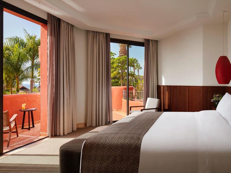 Gemütliches Schlafzimmer mit großem Bett, braunen Vorhängen und Zugang zu Balkon mit Pflanzen.