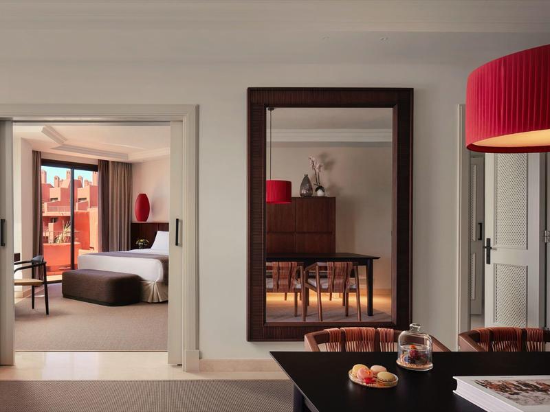 Moderner Wohnraum mit Essbereich, großem Spiegel und Sicht auf Schlafzimmer mit rotem Lampenschirm.