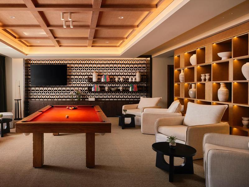 Gemütlicher Spielraum mit rotem Billardtisch, bequemen weißen Sesseln und hellem Holzregal.