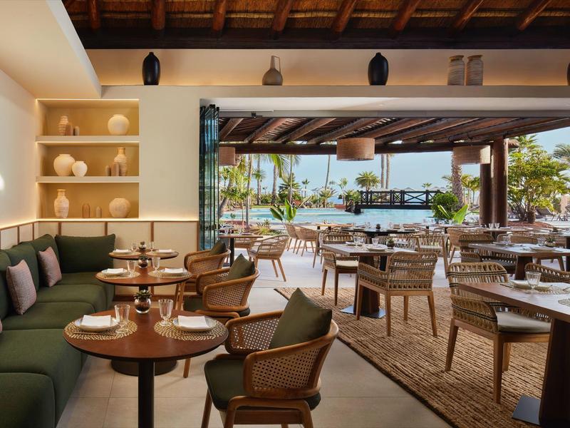 Gemütliches Restaurant mit Holzmöbeln, grünem Sitzbereich und offenem Blick auf Terrasse und Pool.