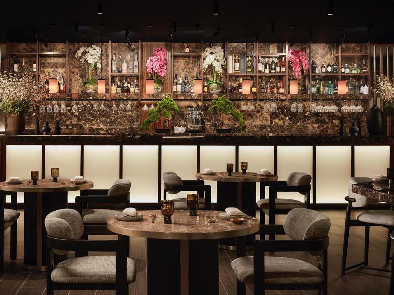 Moderne Restaurant-Innenansicht mit runden Holztischen, schwarzen Stühlen und Deckenbeleuchtung.