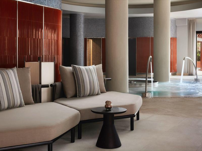 Moderne Lounge mit runden Sofas in Beige, gestreiften Kissen und dunklem Beistelltisch vor Säulen.