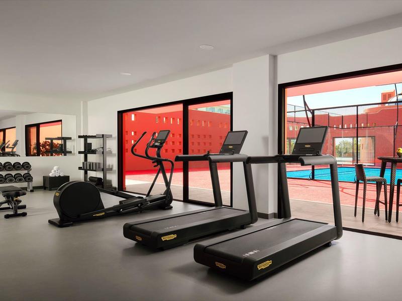 Moderner Fitnessraum mit Laufbändern, Hanteln und großem Fenster zum Außenbereich mit Pool.