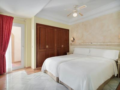 Hotelkamer met twee eenpersoonsbedden, kleine kast en toegang naar balkon of badkamer.