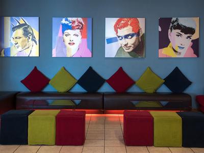 Moderne wachtruimte met kleurrijke kussens en heldere popartportretten aan de muur.