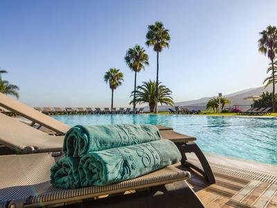 Chaises longues avec serviettes près de la piscine avec des palmiers et un ciel dégagé en arrière-plan.