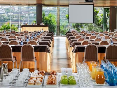 Salle de conférence avec rangées de tables et de chaises, aménagée avec boissons et collations.