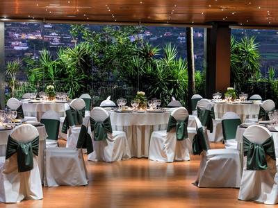 Elegante banketthal met ronde tafels en witte stoelen versierd met groene strikken.