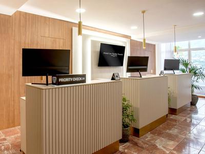 Moderner Hotellobby-Empfang mit Holzvertäfelung und drei Computerstationen auf weißem Tresen.