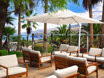 Outdoor-Lounge mit Holzmöbeln und Sonnenschirm mit Blick auf das Meer und Palmen.