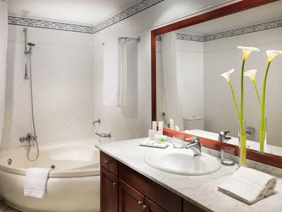 Badkamer met ligbad, douche, wastafel, grote spiegel, handdoek en bloemen.