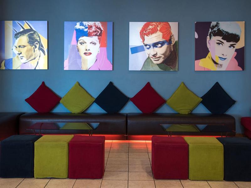 Moderne wachtruimte met kleurrijke kussens en heldere popartportretten aan de muur.