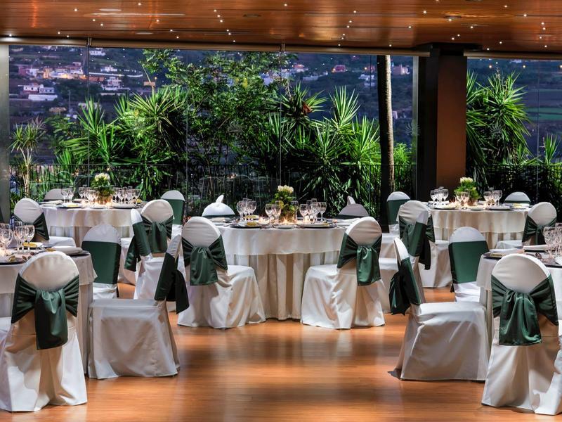 Elegante banketthal met ronde tafels en witte stoelen versierd met groene strikken.