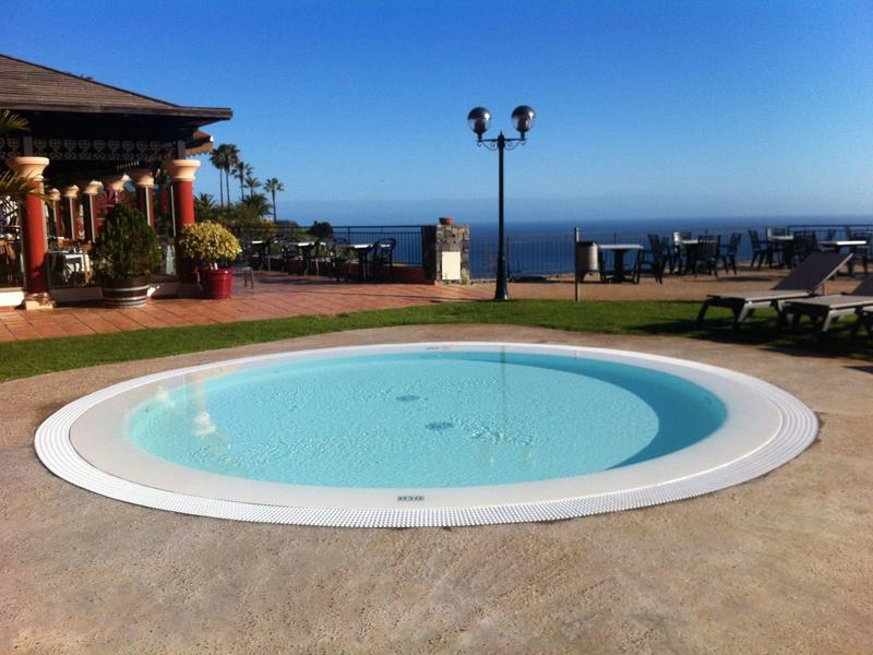 Rond zwembad op terras met uitzicht op zee en blauwe lucht.