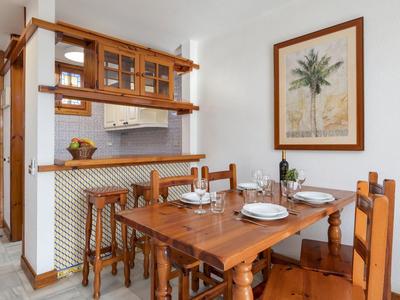 Küchen-Essbereich mit Holzmöbeln, gedecktem Tisch, Bartresen und Pflanzenbild an weißer Wand.