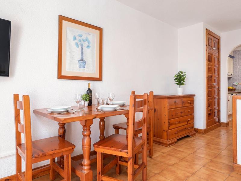 Essbereich mit Holztisch, vier Stühlen, Weinflasche, Bild an der Wand und Sideboard mit Grünpflanze.