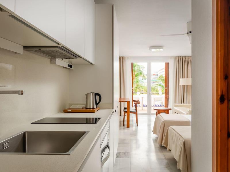 Helle kleine Küche mit Spüle und Kocher, offener Durchgang zum Ess- und Wohnbereich mit Balkon.