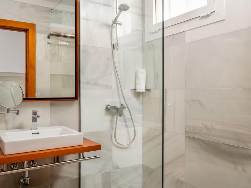 Modernes Badezimmer mit Glasduschkabine, weißem Waschbecken auf Holzablage und großem Spiegel.